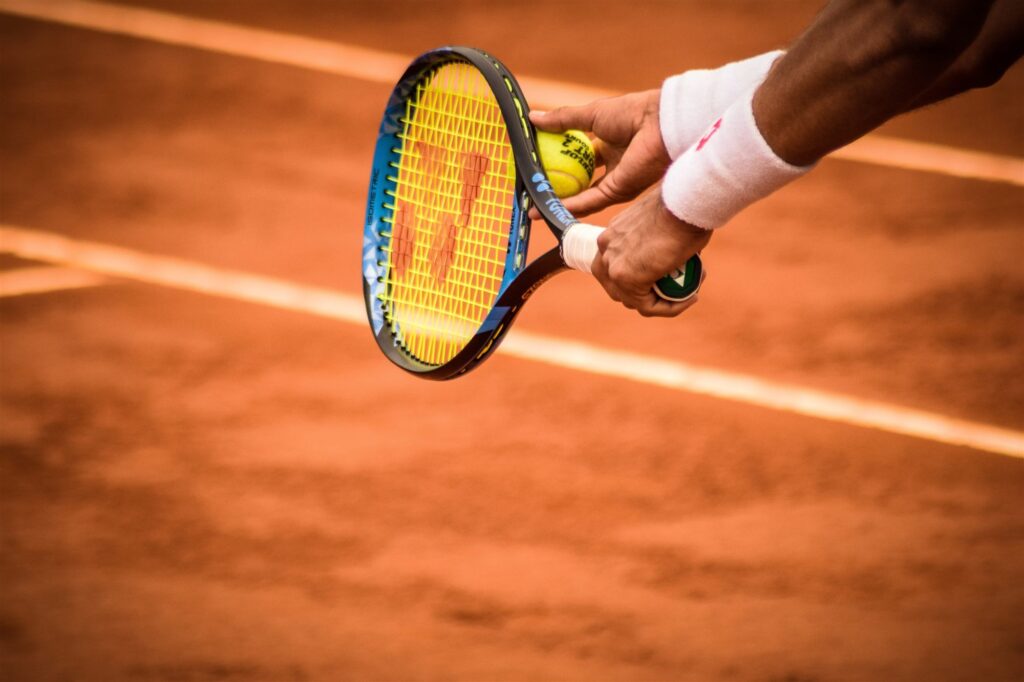Hand mit Tennisschläger und Ball über einem Sandplatz